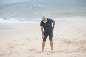 An image of an elderly man holding his leg on the beach