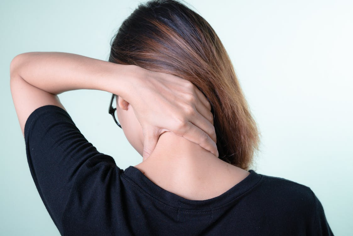 A woman is shown massaging her neck, depicting neck pain.