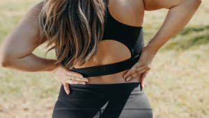 Woman outdoors in athletic wear holding her lower back due to pain